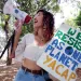 Mitzi Jonelle Tan is outside and talking into a megaphone. She's holding up a sign that says "We Resist As One Planet/YACAP"