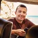 Brian Holguin looks into a car (or cart) and smiles at the camera inside.