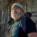Wayne Thompson, who has a gray beard and is wearing a beanie and a backpack, looks off in the distance.