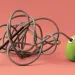 A little green vacuum has long cord tied up in knots against a pink-orange background.