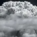 Black-and-white photo shows an enormous white cloud of smoke above trees.
