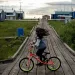 A kid with long hair covering their face rides a bike on a wooden boardwalk. A sign says "Speed Limit 5."