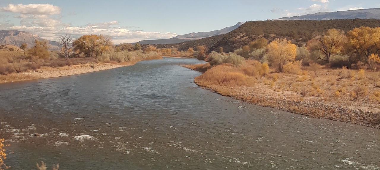 A landscape photo of a river in the western United States with mountains and blue sky in the background.