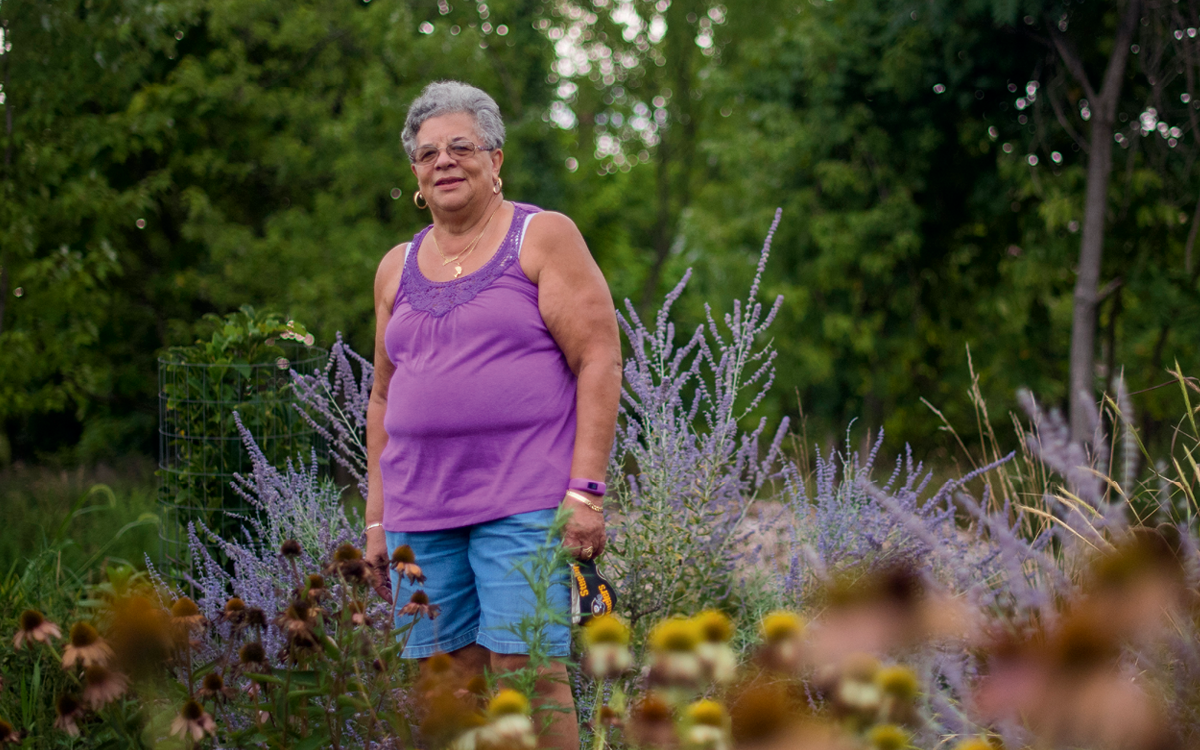 Zinna Scott, wearing a purple tank top, stands in front of a lavender plant and smiles slightly.