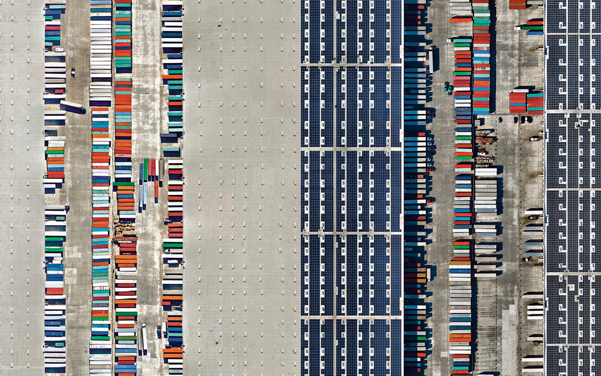 Left aerial photo shows the Westmont Distribution Center in 2014, with concrete around rows of colorful storage containers. Right aerial photo shows the center with large, dark-blue solar arrays replacing the concrete in 2017.