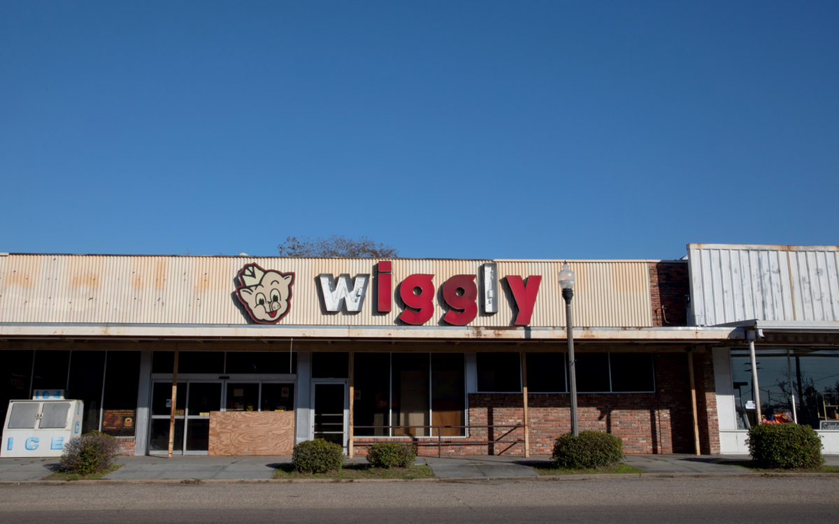 Exterior of a dilapidated Piggly Wiggly grocery store. Two of the red letters of the "Wiggly" sign are broken.