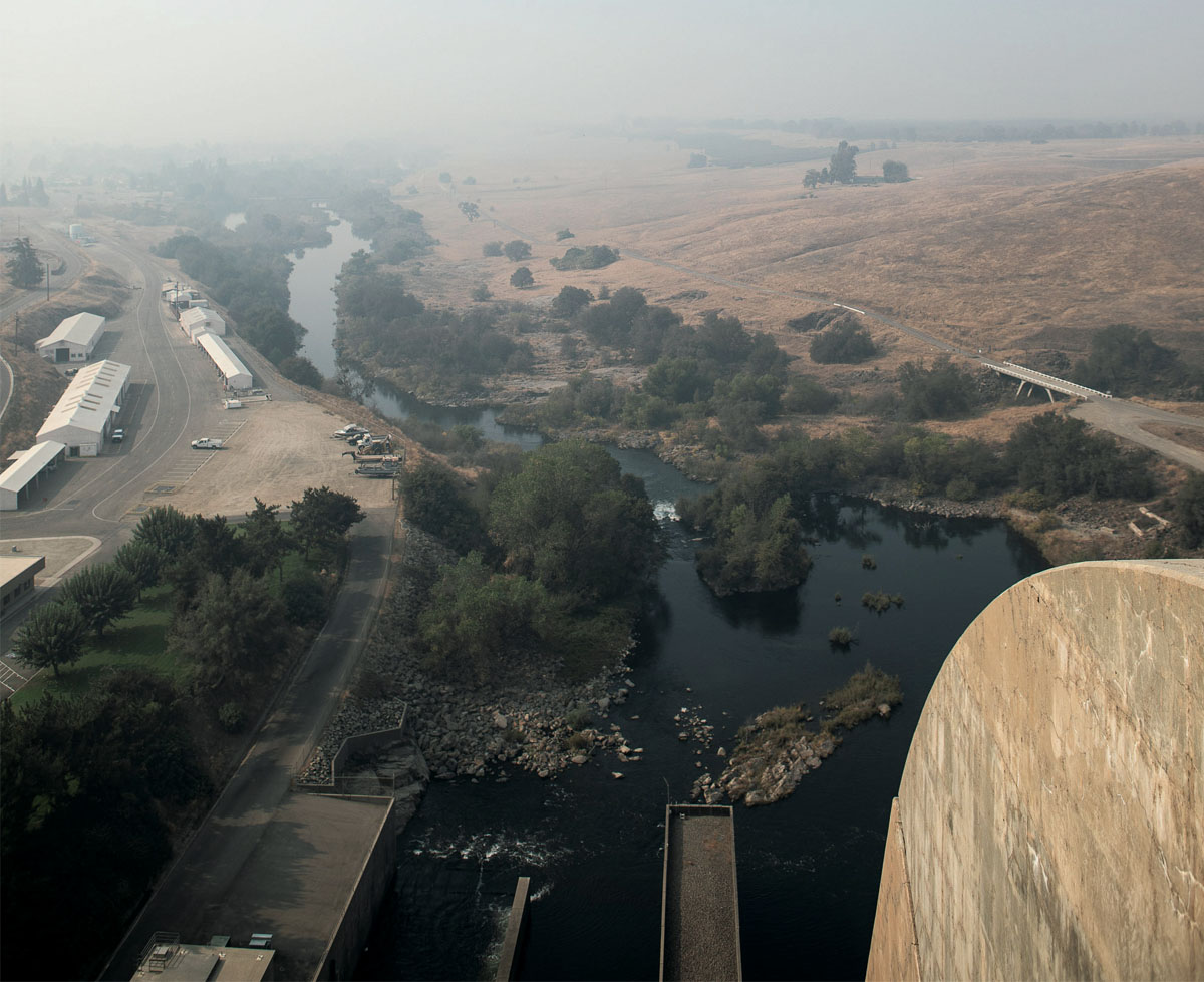 View from atop Friant Dam shows Millerton Lake and dry grassland. The air is smoky.