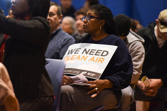 Activist Vicki Dobbins holds a \"Clean Air\" sign while seated at last night&#039;s public hearing for the Marathon proposal.  The hearing took place in Detroit&#039;s River Rouge neighborhood.