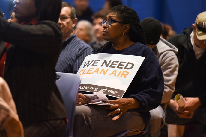 Activist Vicki Dobbins holds a \"Clean Air\" sign while seated at last night's public hearing for the Marathon proposal.  The hearing took place in Detroit's River Rouge neighborhood.