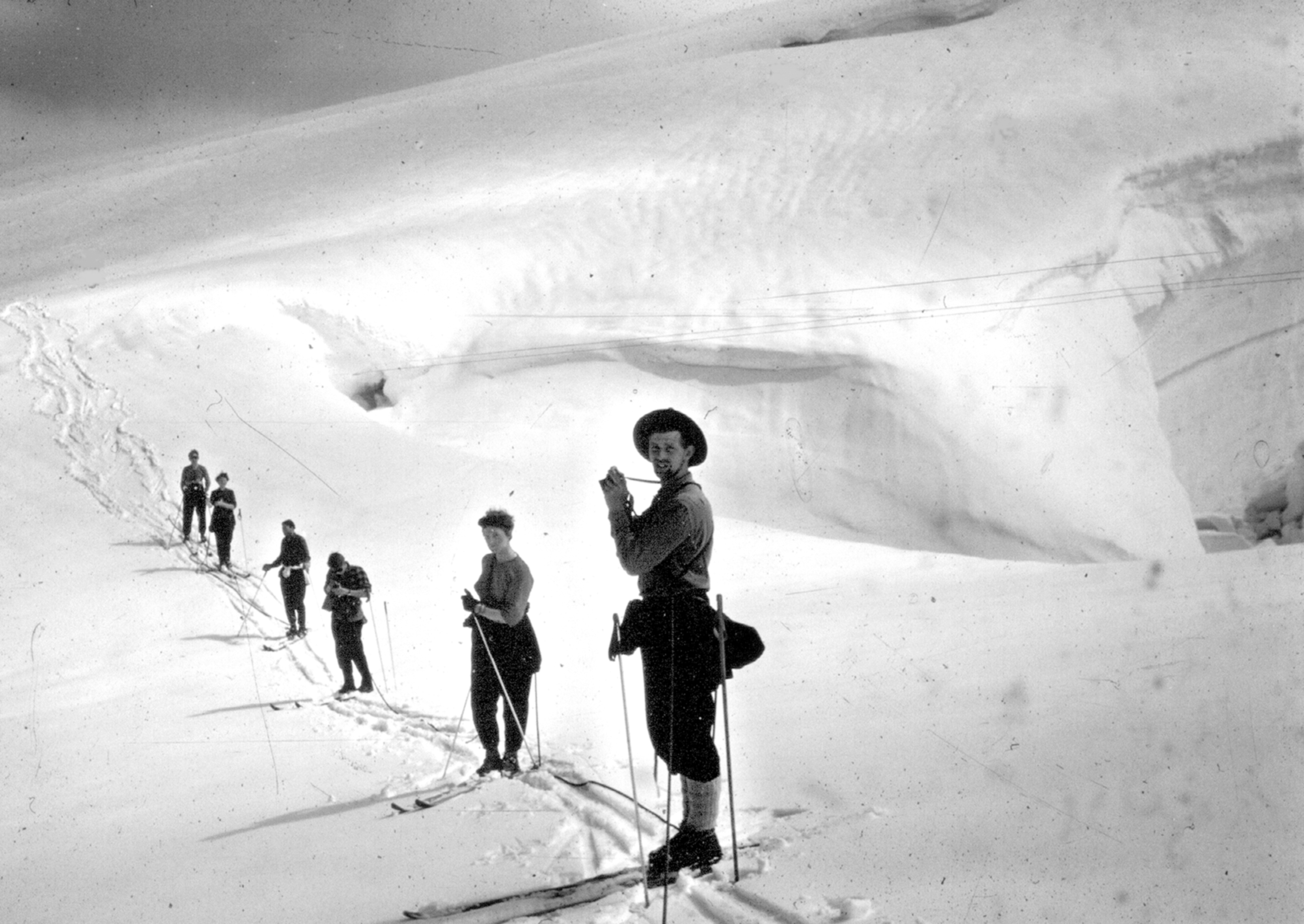 Black and white photo of a row of skiers against the background of a blindingly white glacier, taken in the 1950s.