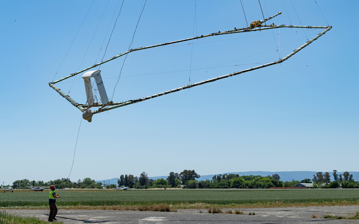 Helicopter against a blue sky with a metal frame hanging below it. 