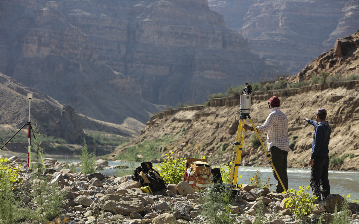 Two people with survey equipment stand on the side of the river.