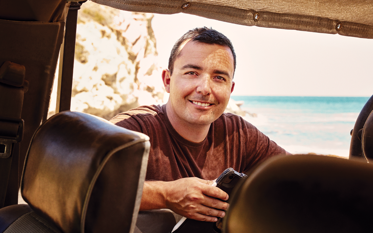 Brian Holguin looks into a car (or cart) and smiles at the camera inside.
