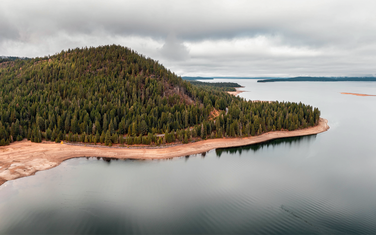 Lake Almanor with a tree-lined shoreline and gray, cloudy skies above.