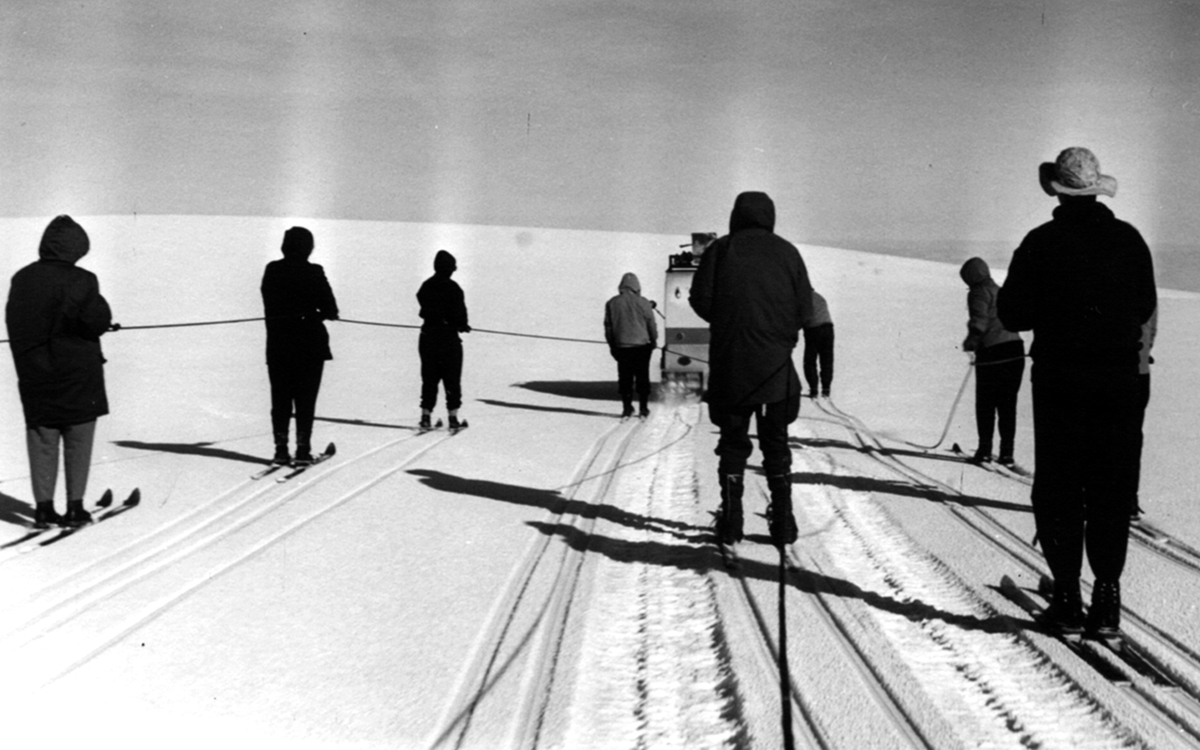 Black and white photo of a row of skiers against the background of a blindingly white glacier, taken in the 1950s.