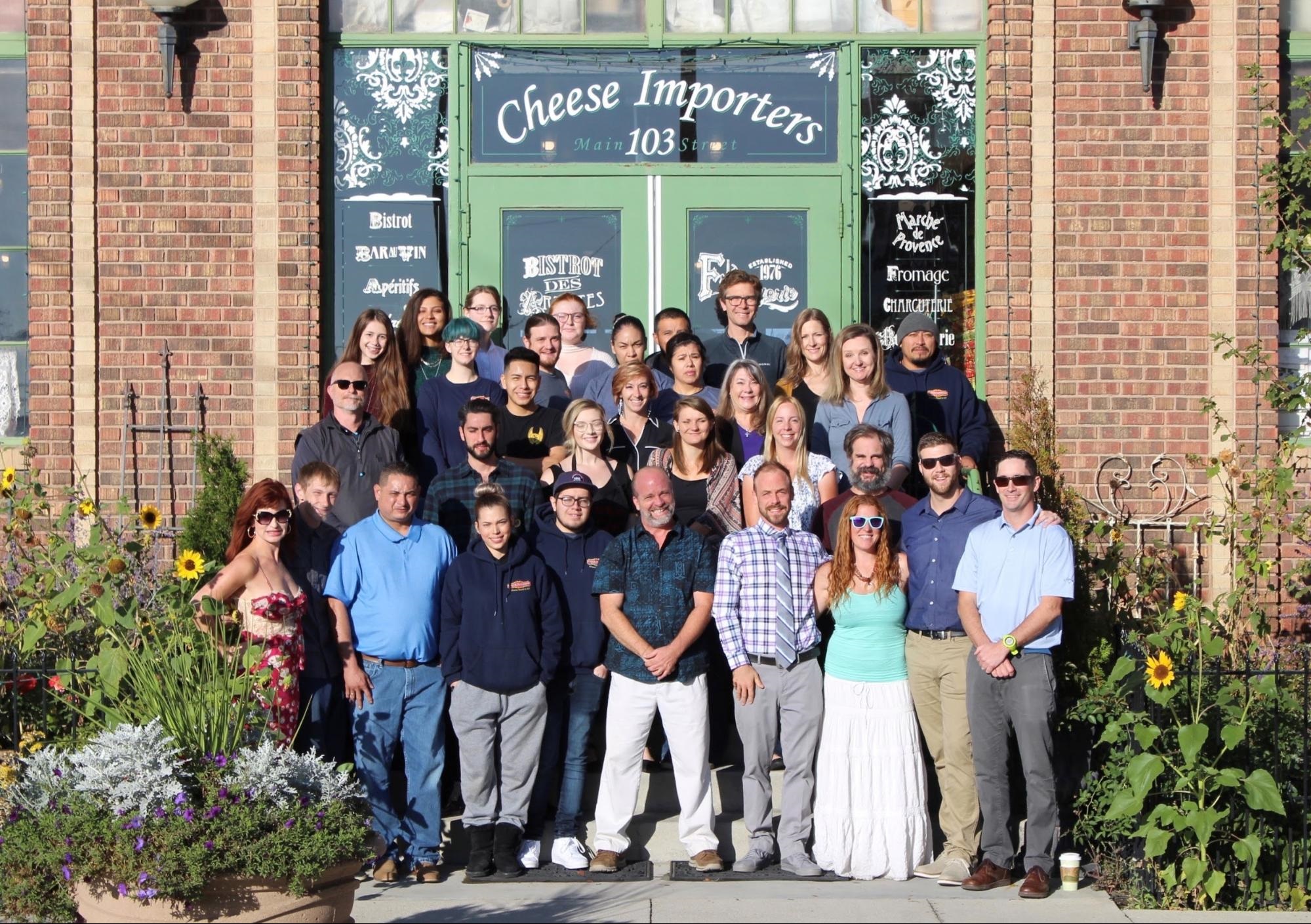The staff of Cheese Importers Warehouse stands in front of the mint-green doors of their store. 