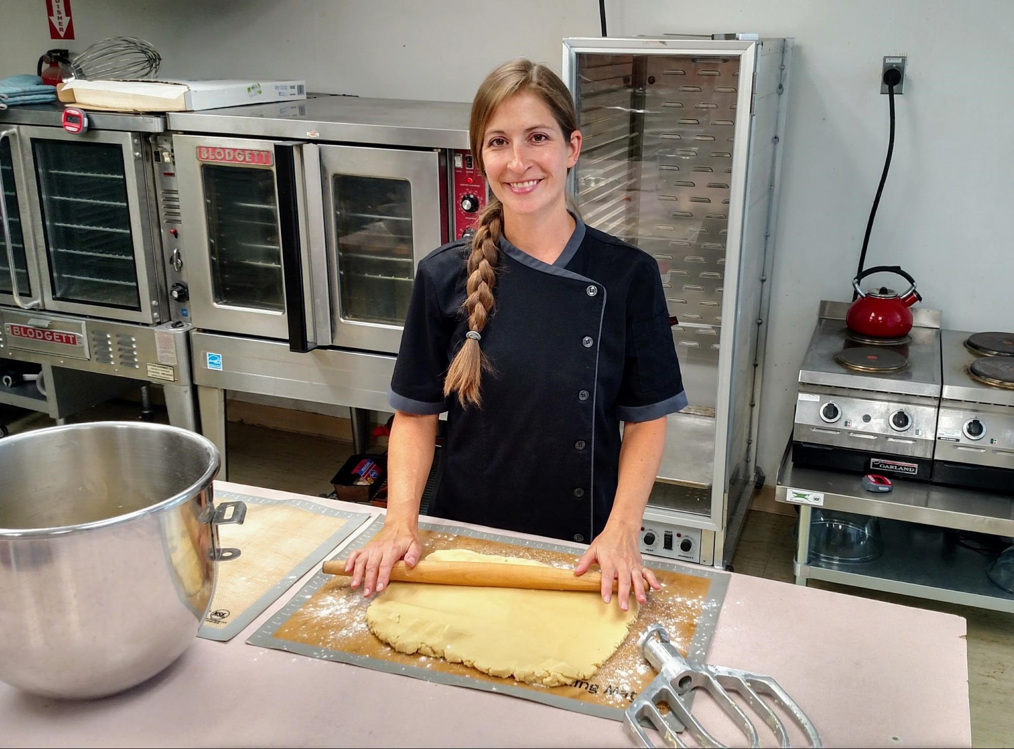Elizabeth Meyers, Chef and Owner of I d’Eclair! Pastry, stands above a sheet of dough with rolling pin in hand.
