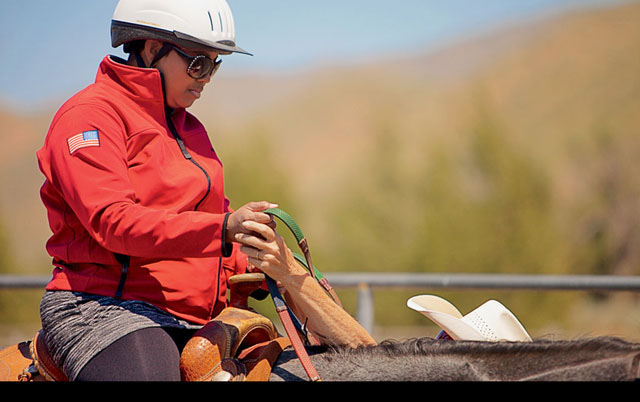 On horseback, La'Sonda White steers a herd of cows into a pen.