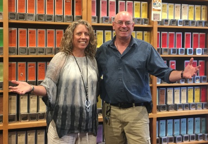 Kari Grady Grossman and George Grossman, Owners of Happy Lucky’s Teahouse, stand together with their arms out in front of shelves of tea