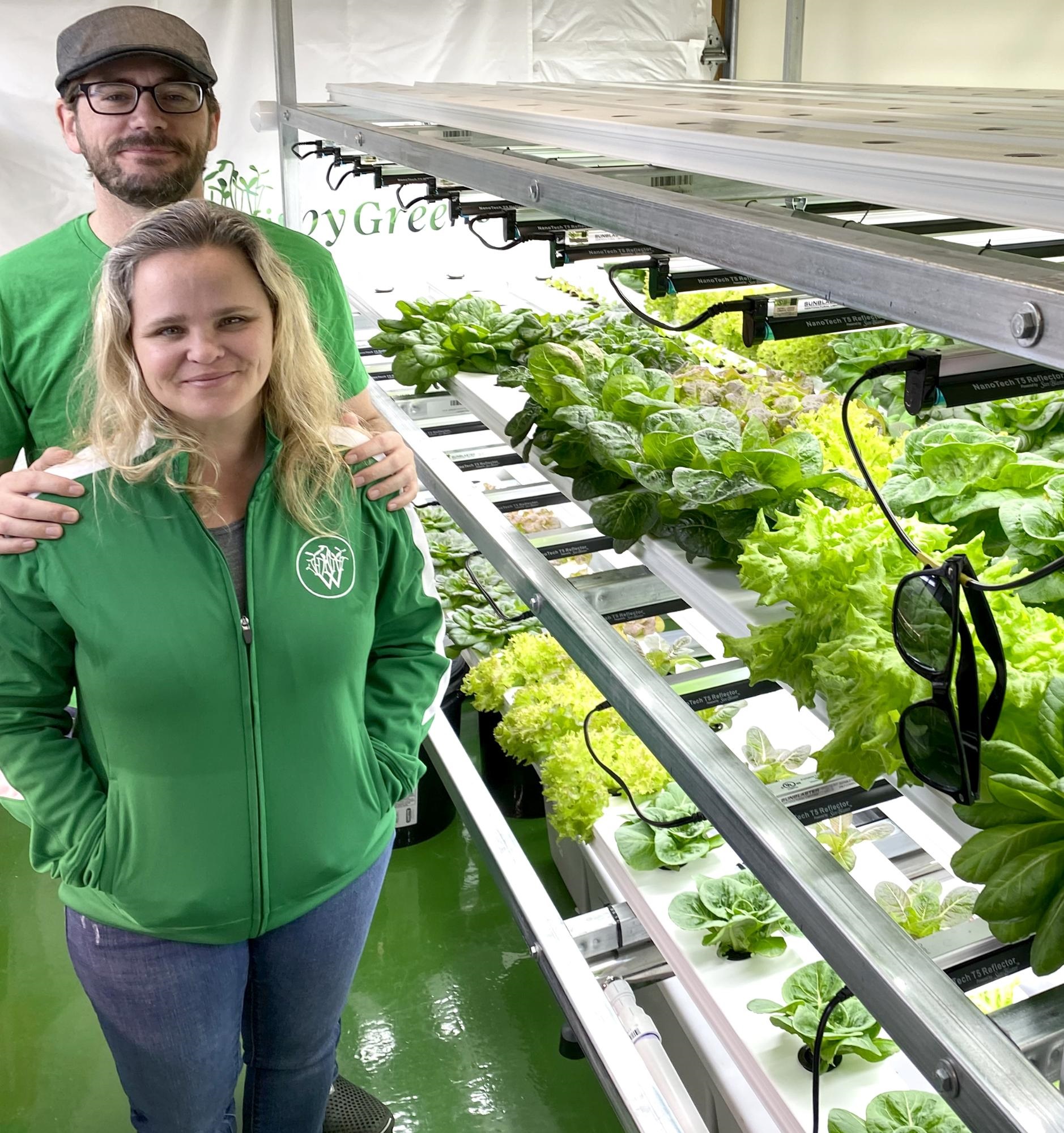 Alicia Beeson (front), Business Manager, Oaken Beeson (back), Owner and Master Grower, stand in front of their hydroponic greens-growing operation.