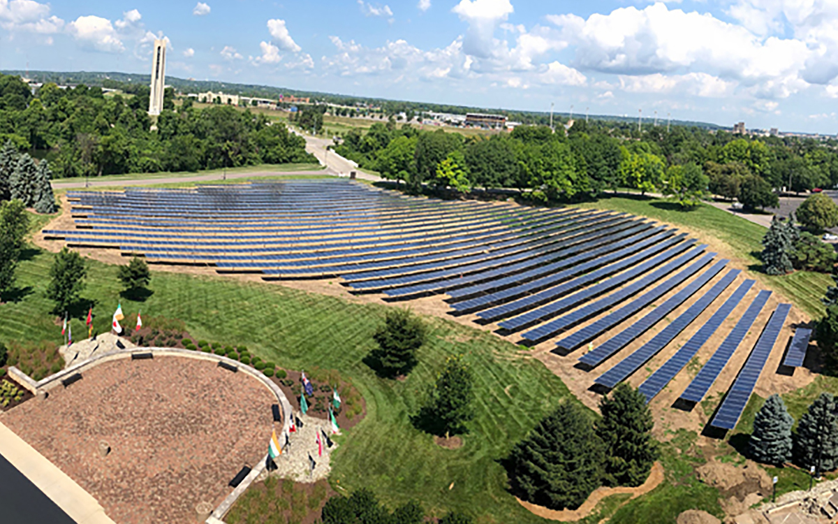 A large solar array sits on a lawn surrounded by trees in the middle of campus.