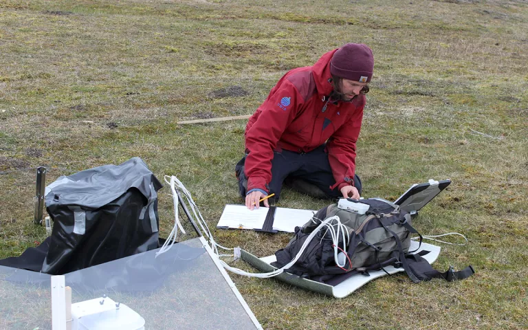 A scientists measures an open top chamber in the field.